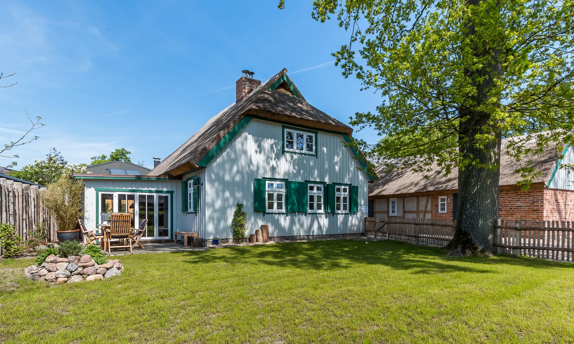 Reetgedecktes Haus mit grünen Fensterläden, Terrasse und großem Garten.