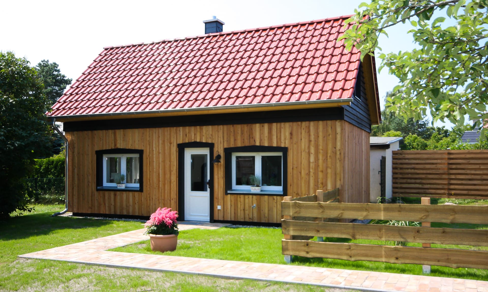 Ein Haus mit Holzfassade, roten Dachziegeln, davor grüner Rasen.