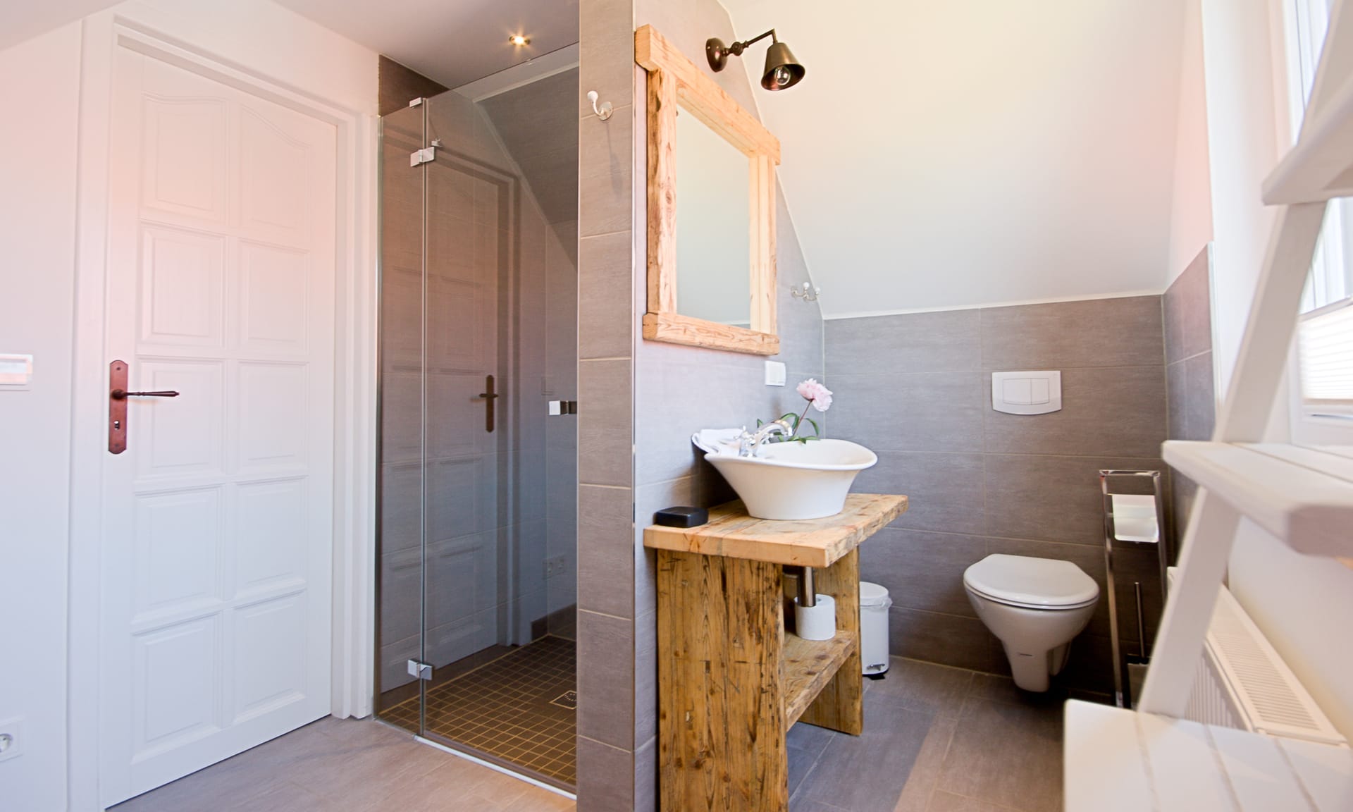 Badezimmer: links die Dusche, rechts Toilette, Waschbecken mit Spiegel, ein Fenster.