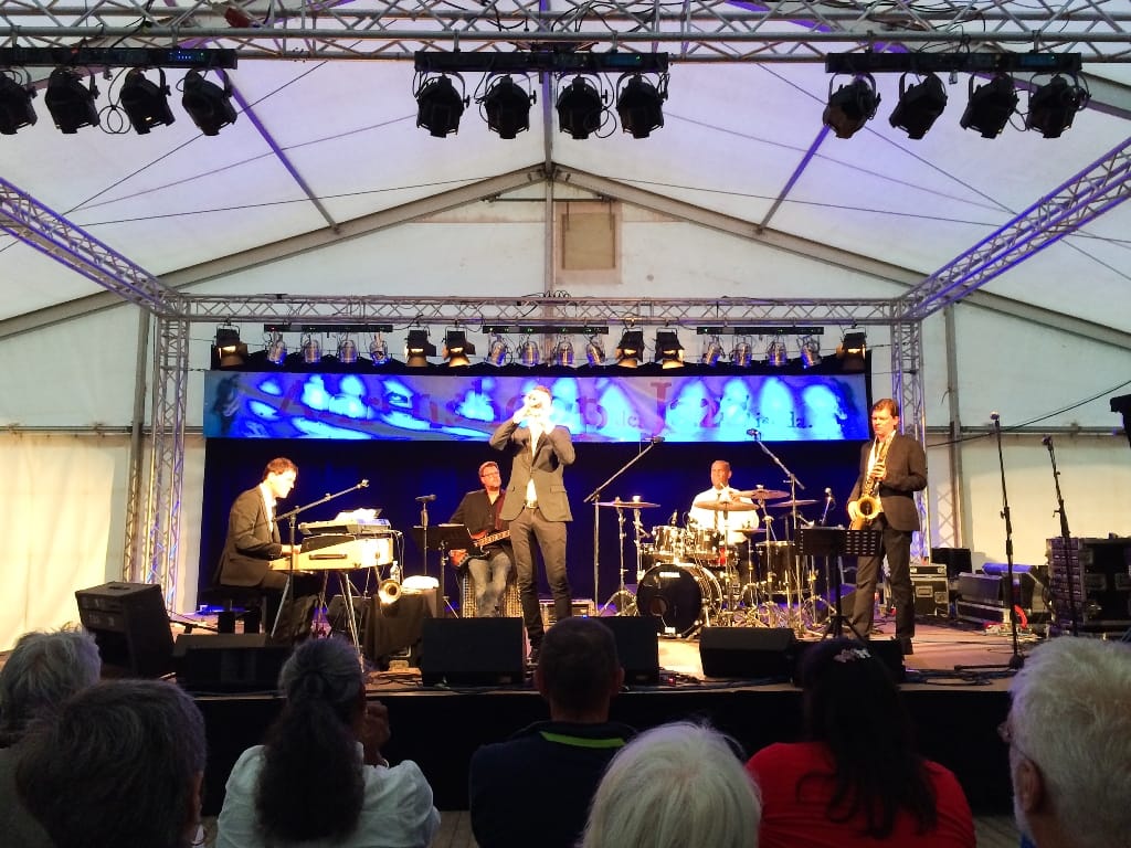 Eine Band spielt live Musik auf einer Bühne unter einem Festzelt vor Zuschauern.