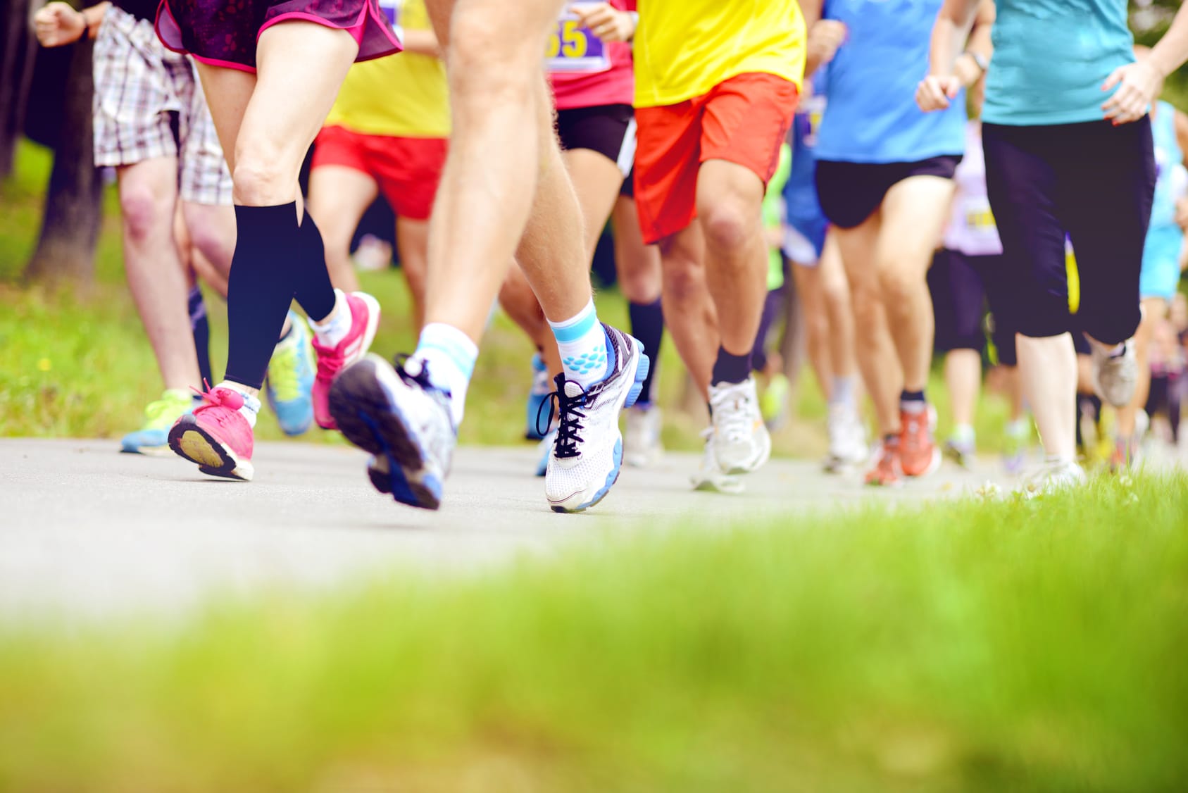 Viele Läuferfüße in bunten Sportschuhen auf einer asphaltierten Straße vor unscharfem Hintergrund.