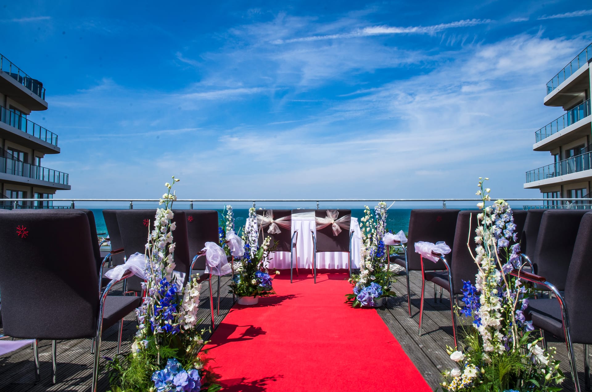 Geschmückter Balkon für eine Hochzeit. Stühle mit weißen Schleifen und Blumen dekoriert, in der Mitte ein roter Teppich.