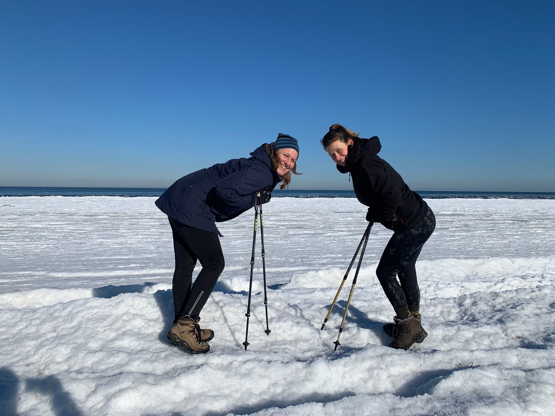 Zwei Frauen mit Nordic-Walking-Stöcken auf einem verschneiten Strand.