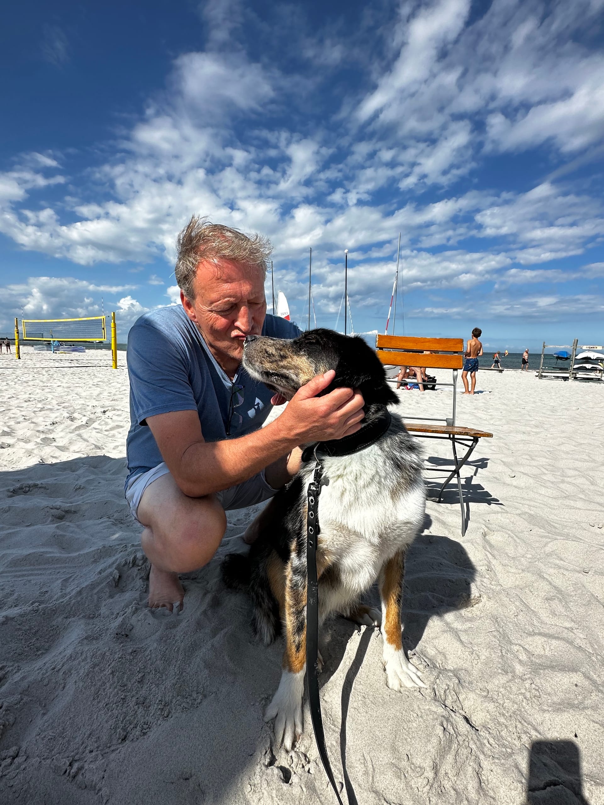 Ein Mann kuschelt mit dem Hund am Strand.