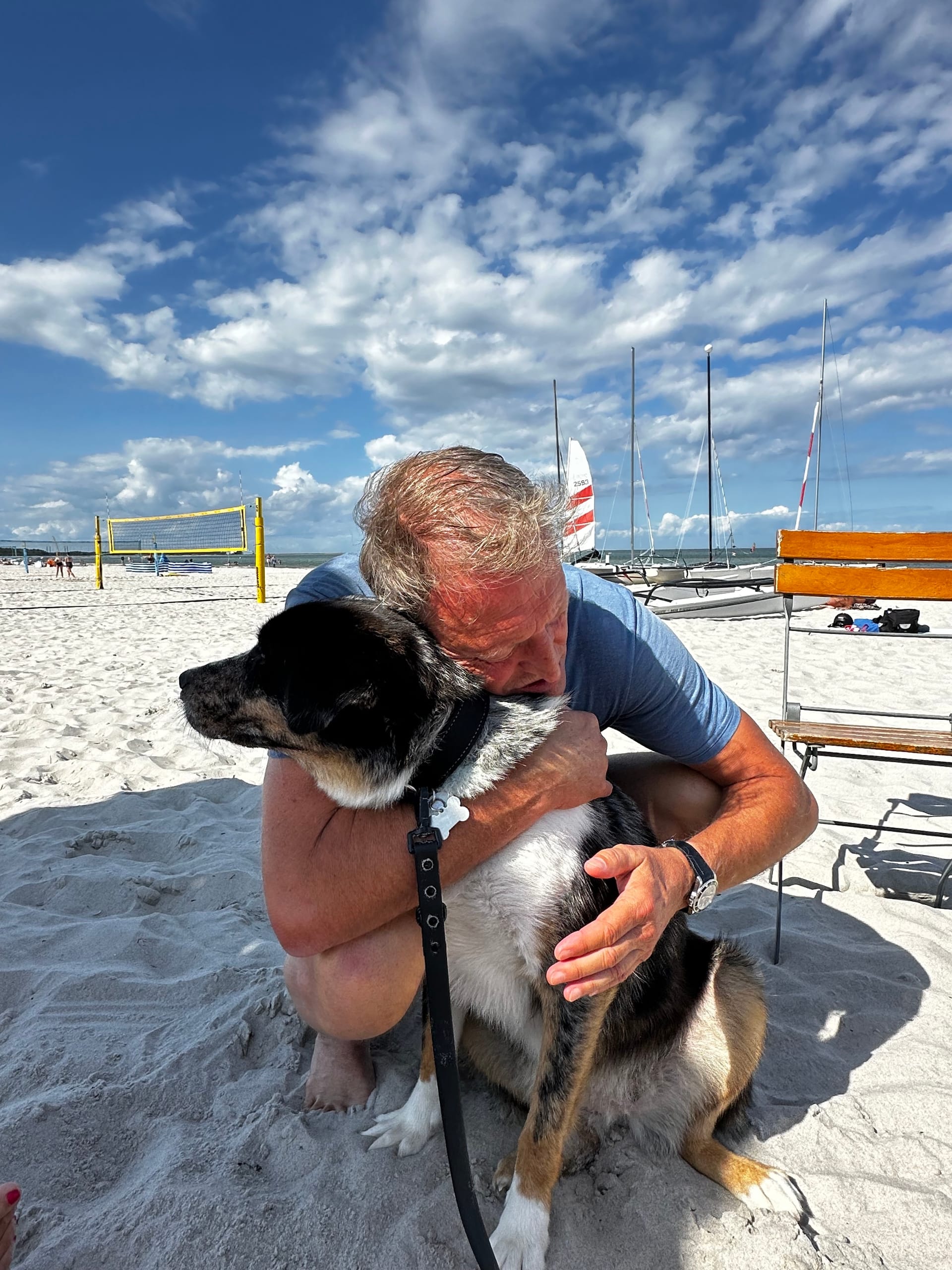 Ein Mann kuschelt mit dem Hund am Strand.
