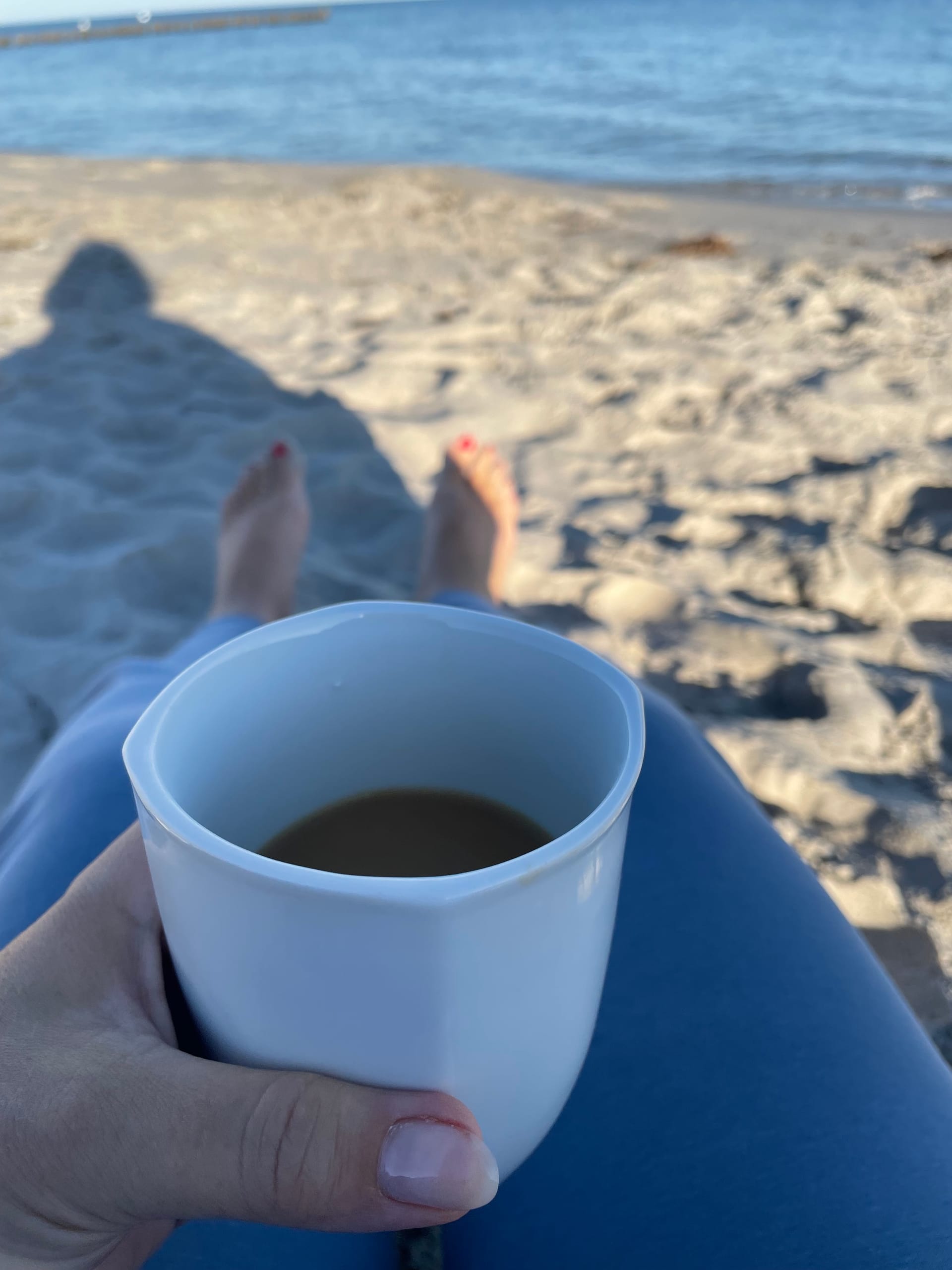 Jemand hält eine Tasse Kaffee, im Hintergrund Strand und Meer.