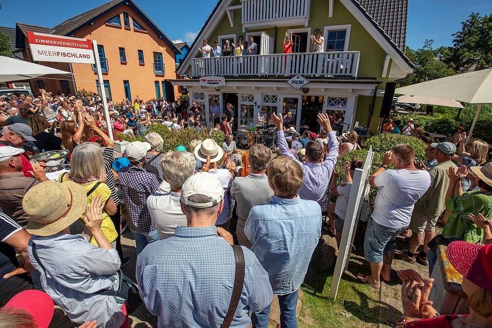 Eine Menschenmenge applaudiert einer Band vor einem grünen Haus mit Balkon.