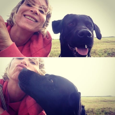 Eine lächelnde Frau macht ein Selfie im Freien mit ihrem schwarzen Labrador Retriever, der ihr im unteren Bild einen Kuss gibt.