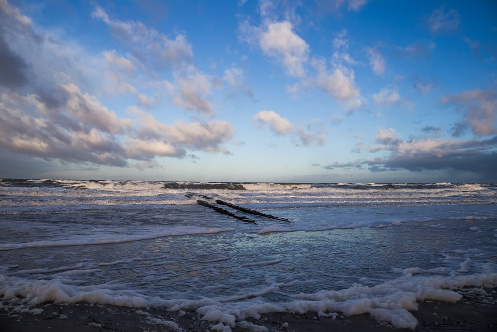 Hohe, schäumende Wellen der Ostsee während eines Sturms am Strand unter grauem Himmel.