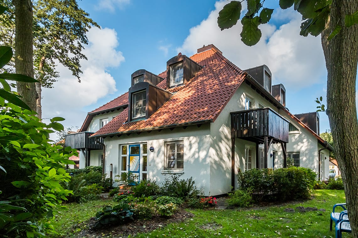 Ein weißes Haus im Garten, mit verzierten Türen. Grüner Umgebung.