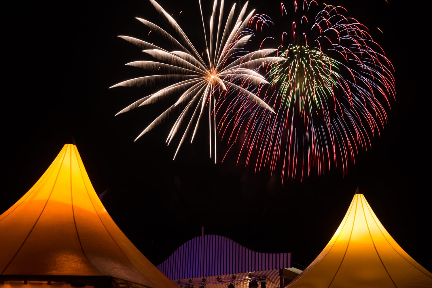 Am Nachthimmel über zwei beleuchteten Partyzelten explodiert ein großes, farbenfrohes Feuerwerk.