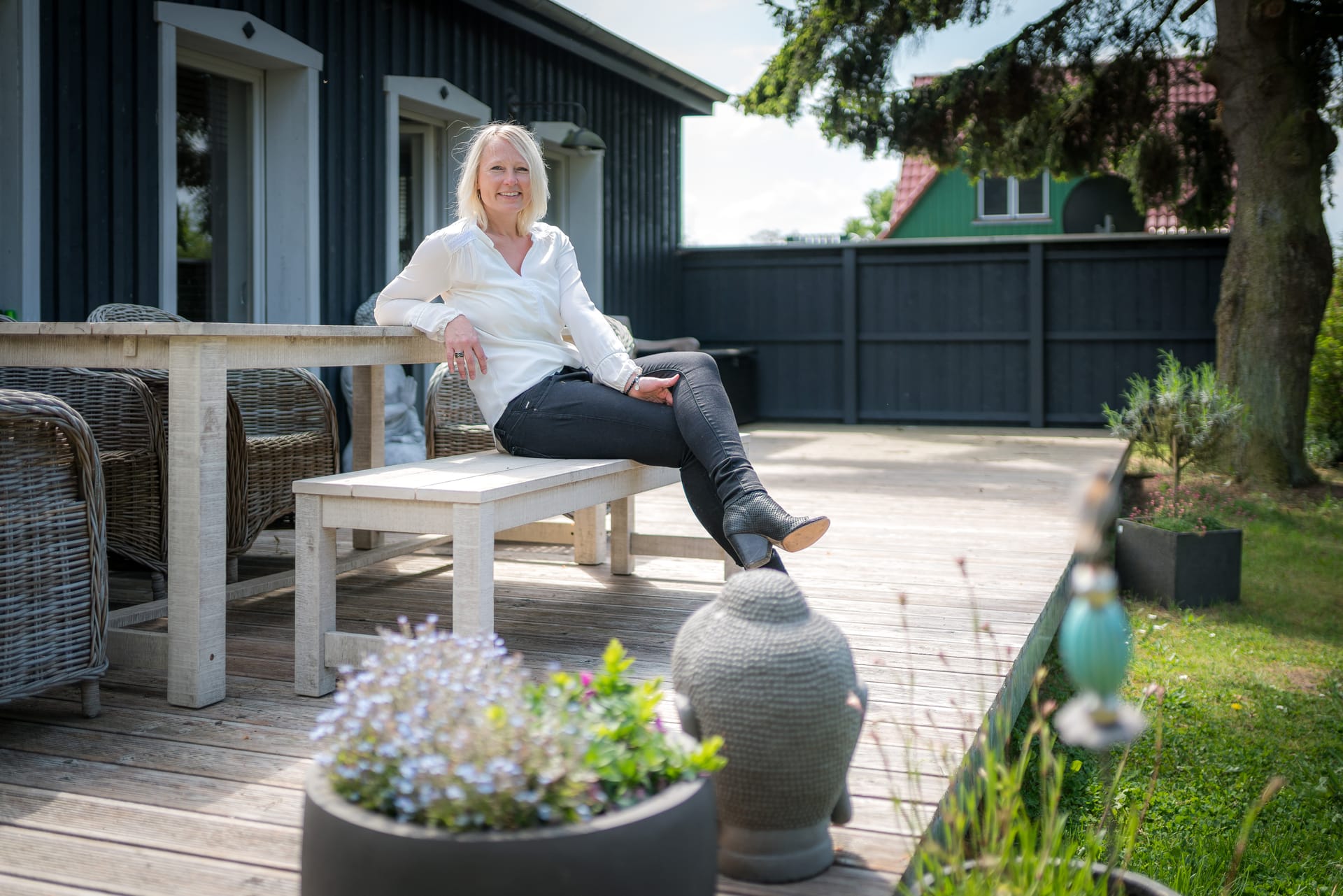 Eine Frau sitzt auf der Bank auf der Terrasse und lächelt.