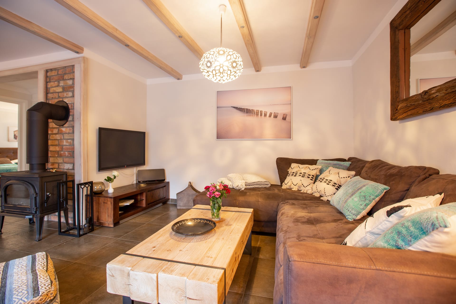 Ein gemütliches Wohnzimmer mit Kamin, Ecksofa mit Dekokissen und Holztisch.