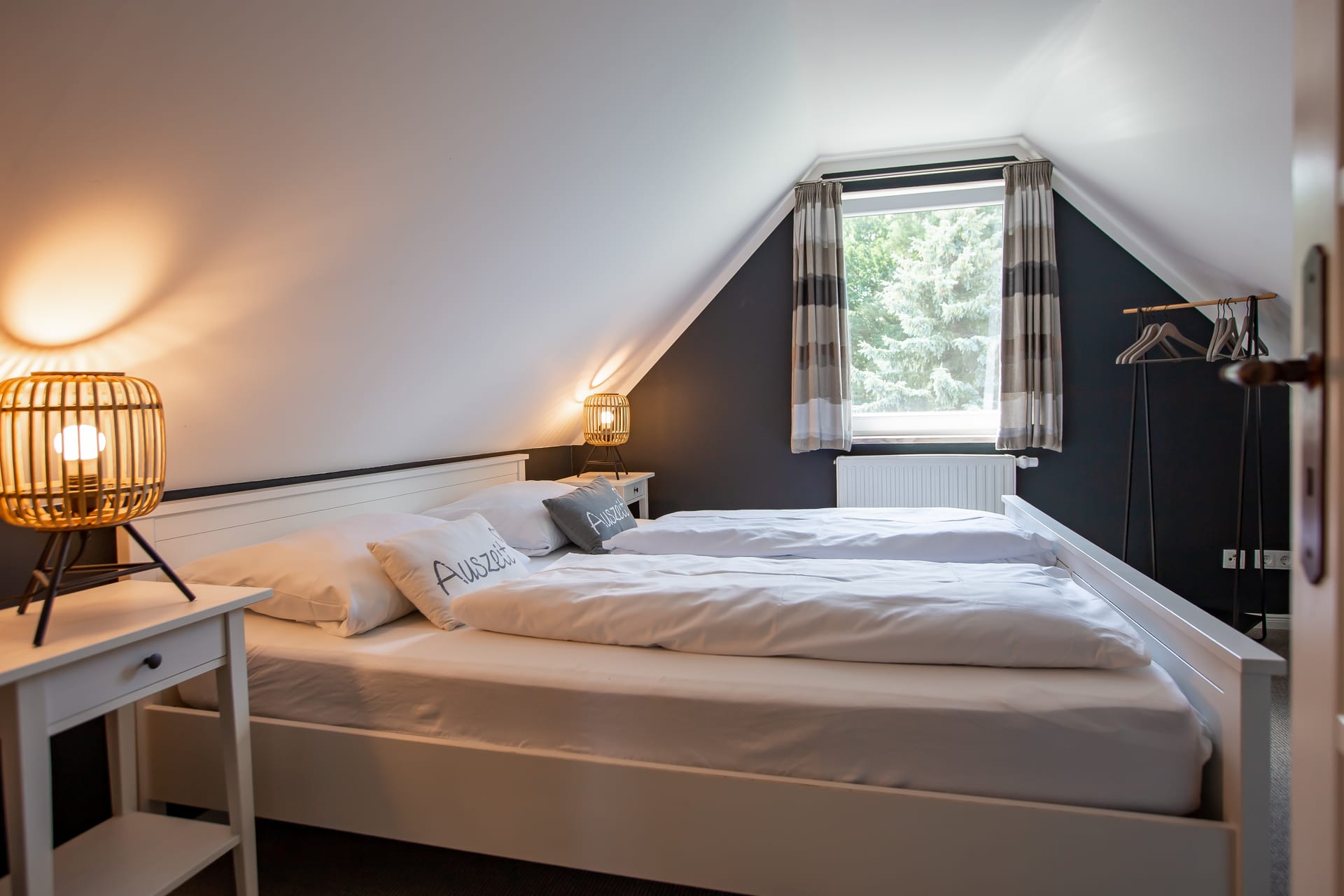 Schlafzimmer unter der Dachschräge mit Doppelbett, zwei Nachttischen und dunkelblauer Wand.