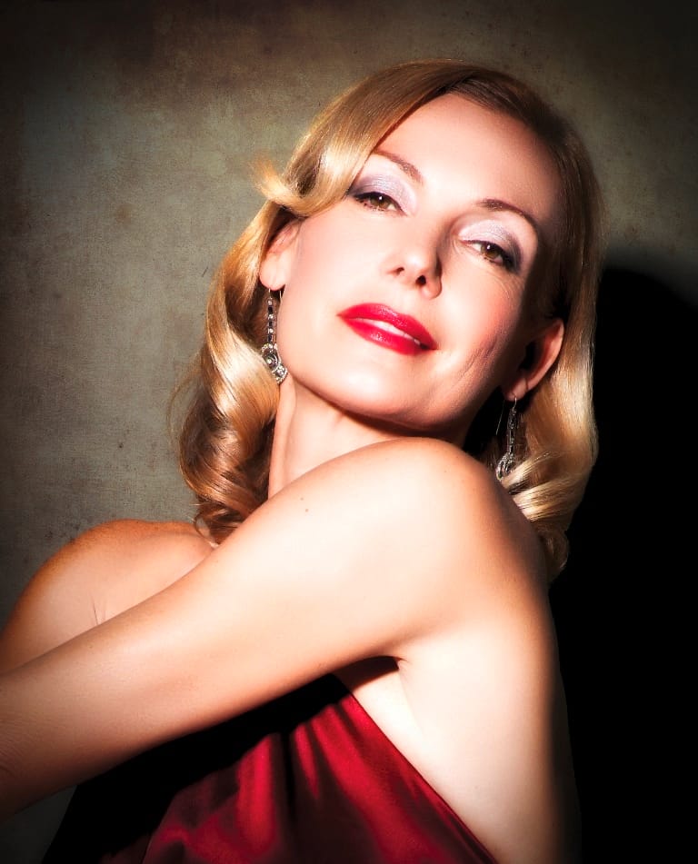 Eine blonde Frau mit roten Lippen blickt lächelnd nach oben.