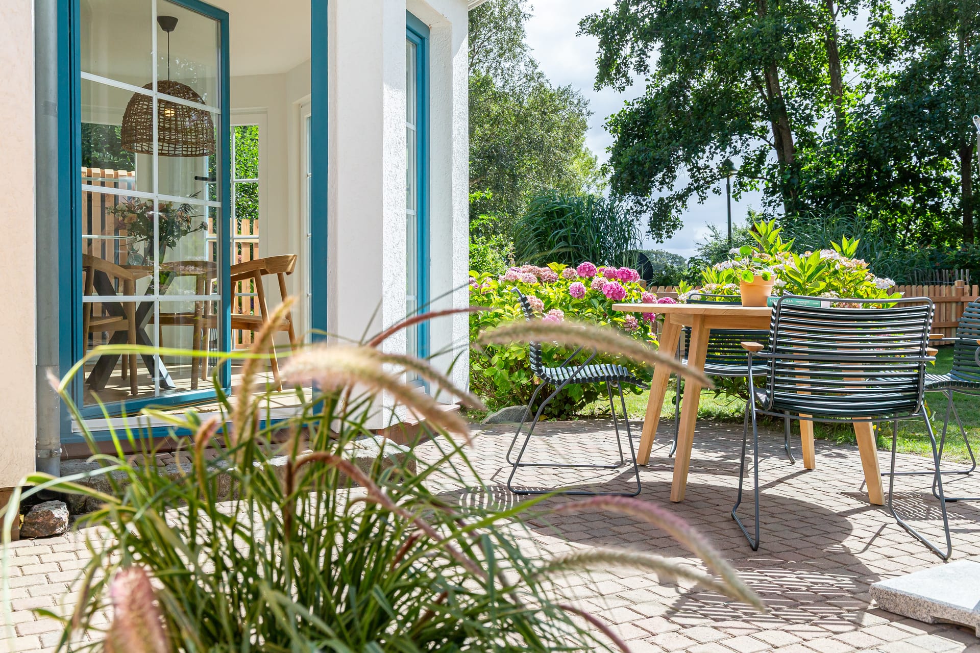 Sonnige Terrasse mit Tisch, Stühlen und blühendem Garten am Ferienhaus