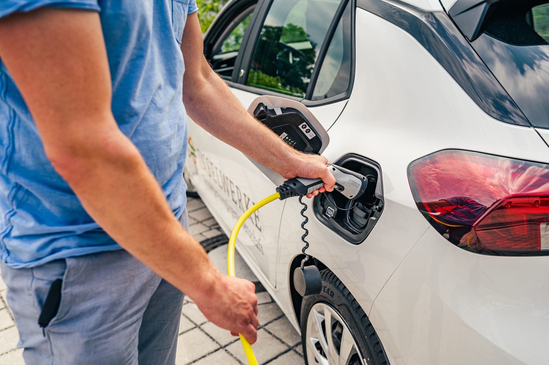Person lädt ein Elektroauto mit Ladekabel an einer öffentlichen Ladesäule auf.