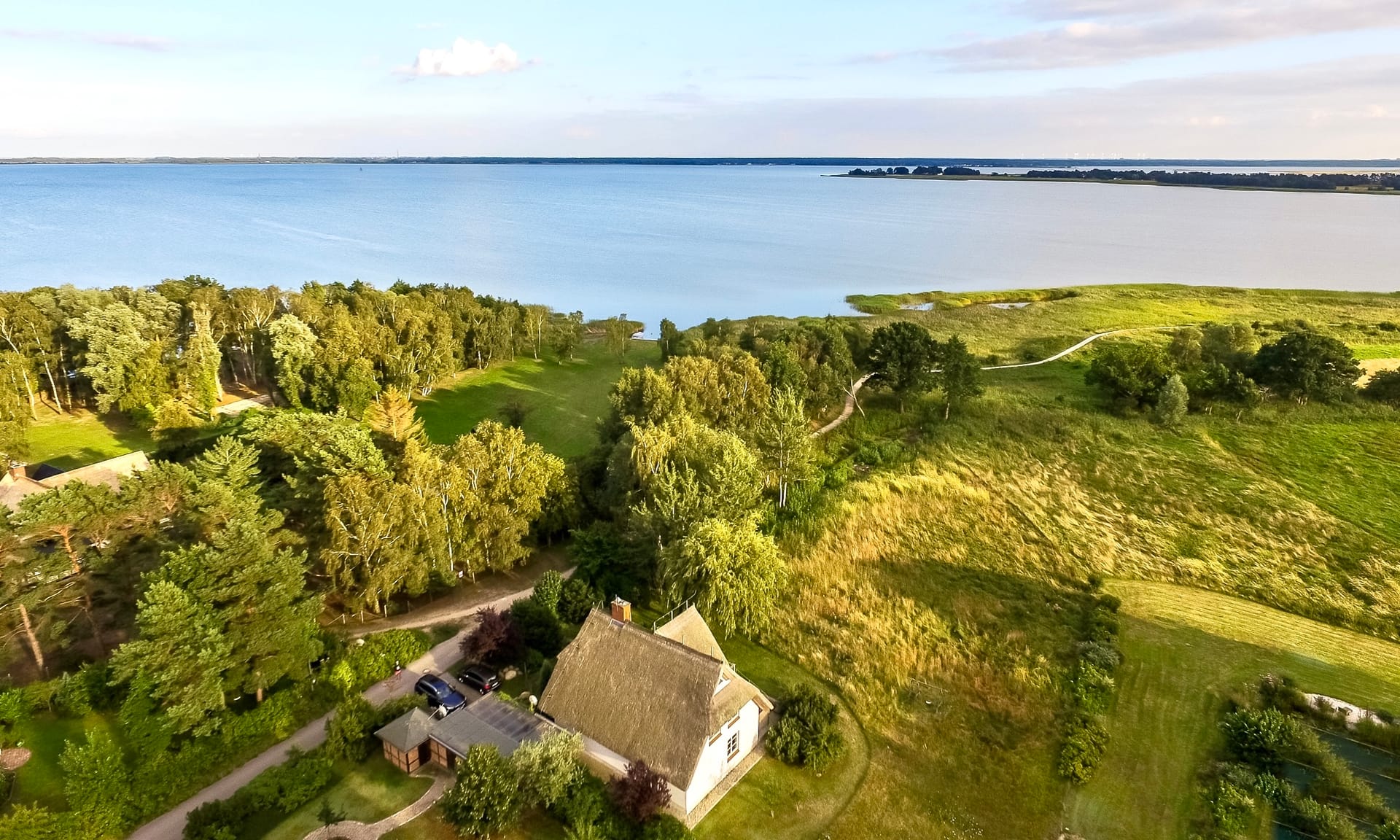 Luftaufnahme eines Reetdachhauses am Bodden mit Wiesen und Wasser