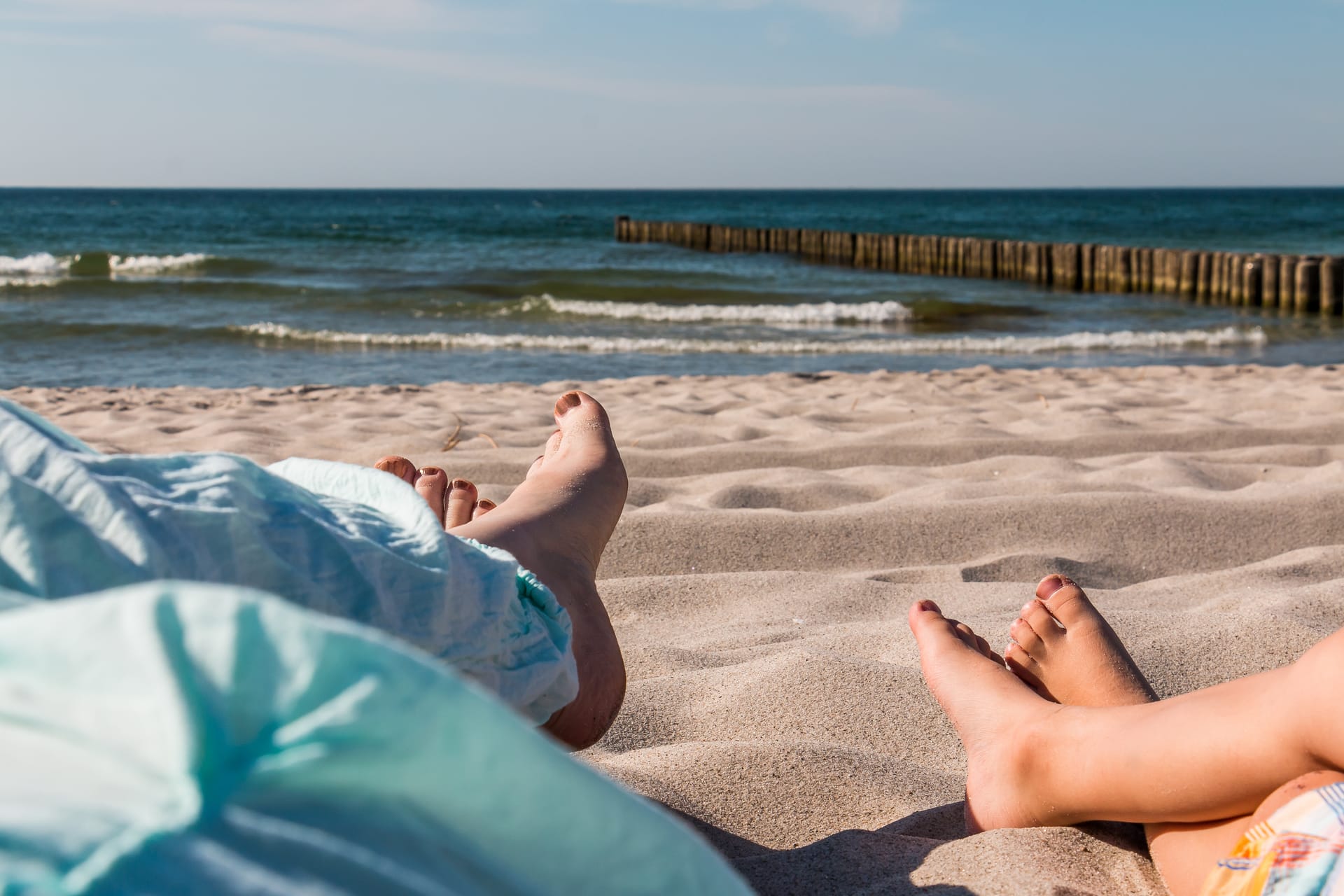 Zwei Personen entspannen barfuß im Sand mit Blick auf die Ostsee