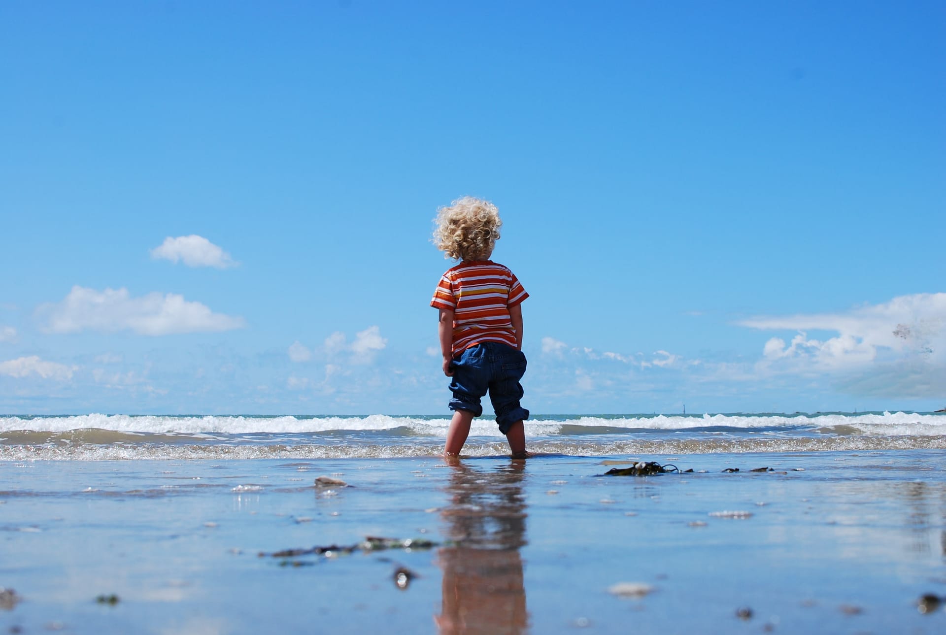 Kleines Kind steht barfuß am Strand und blickt auf die Ostsee