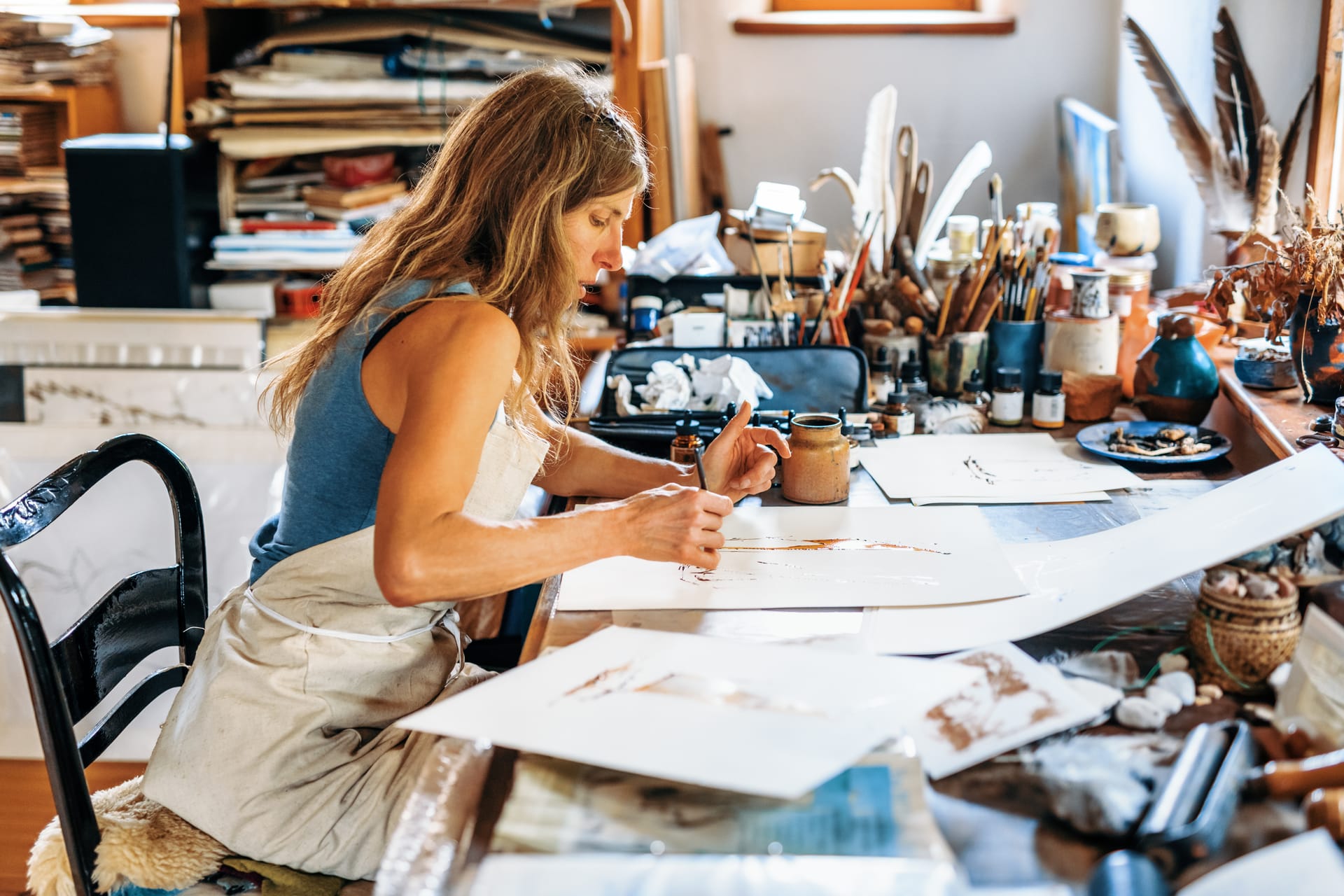 Frau malt konzentriert an einem Tisch in einem lichtdurchfluteten Atelier