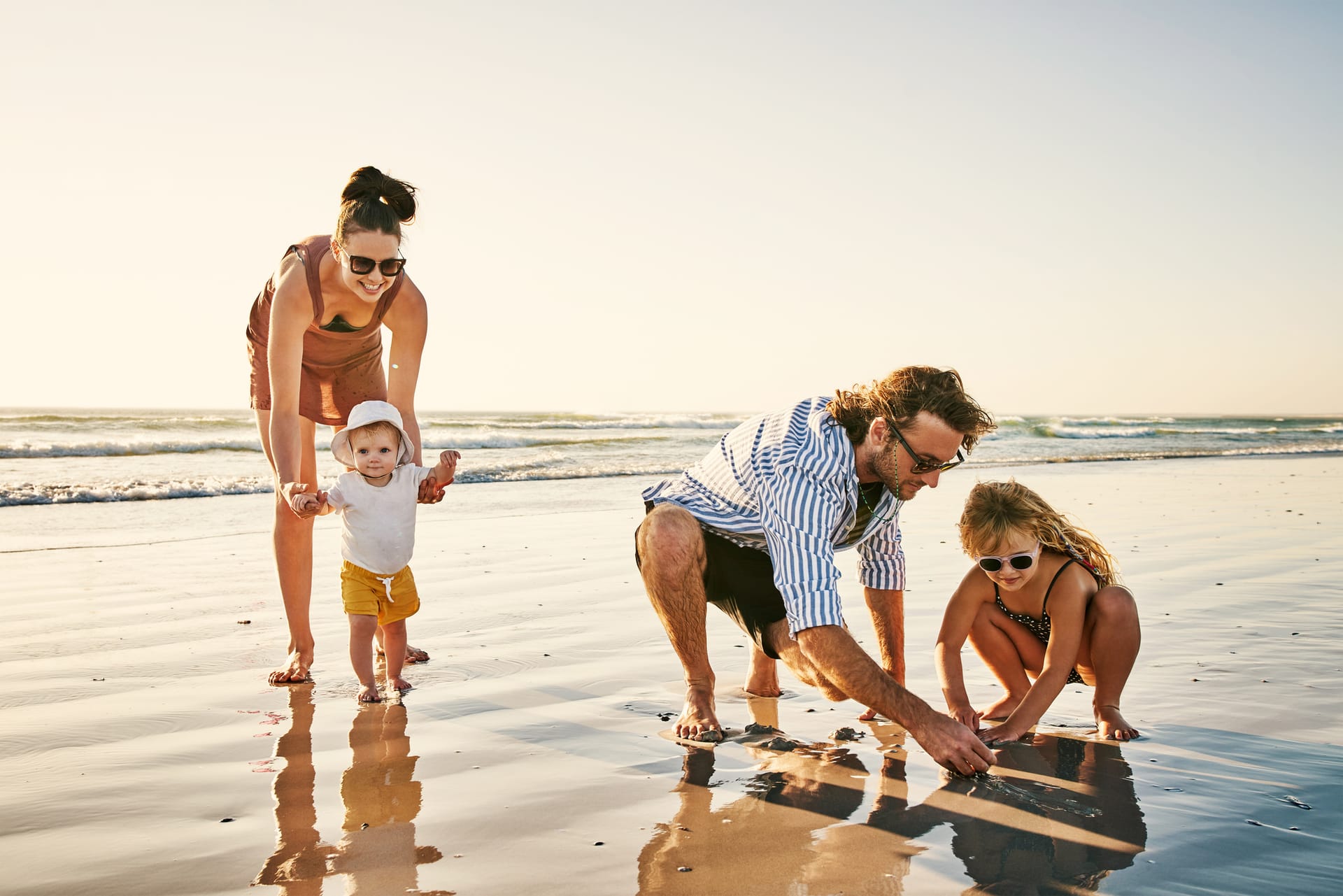 Familie mit zwei Kindern spielt barfuß am Strand bei Sonnenschein
