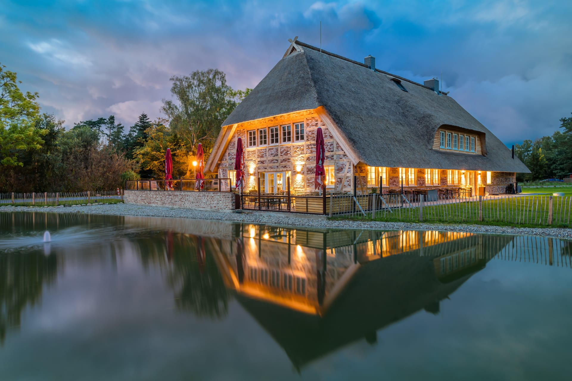 Reetdach-Restaurant am Abend mit Spiegelung im Wasser