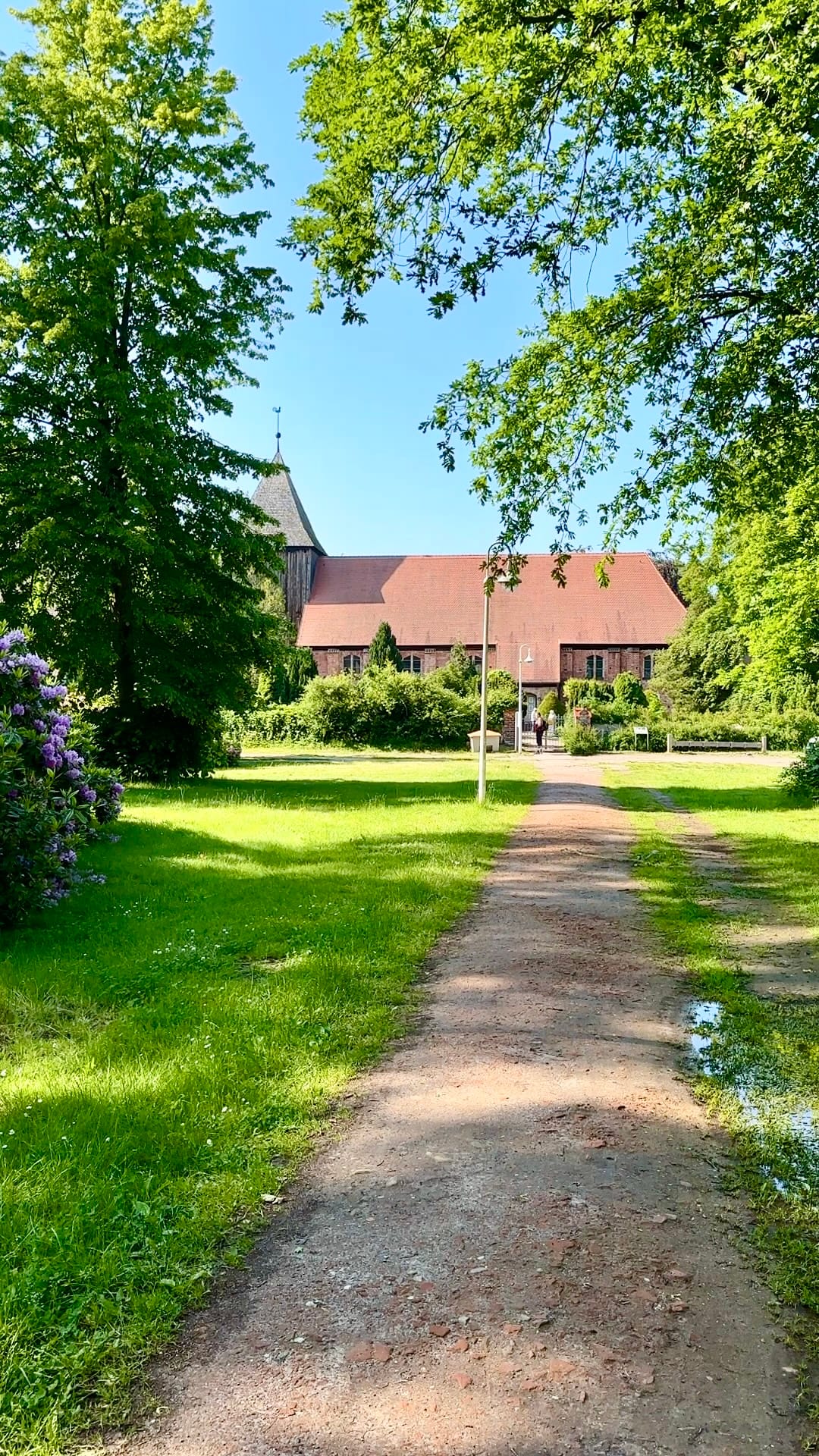 Kirche im Grünen mit Weg durch Parklandschaft im Sonnenschein