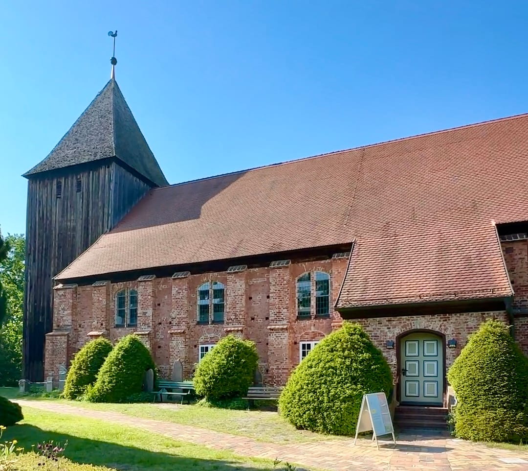 Historische Backsteinkirche mit Holzturm und gepflegtem Kirchhof