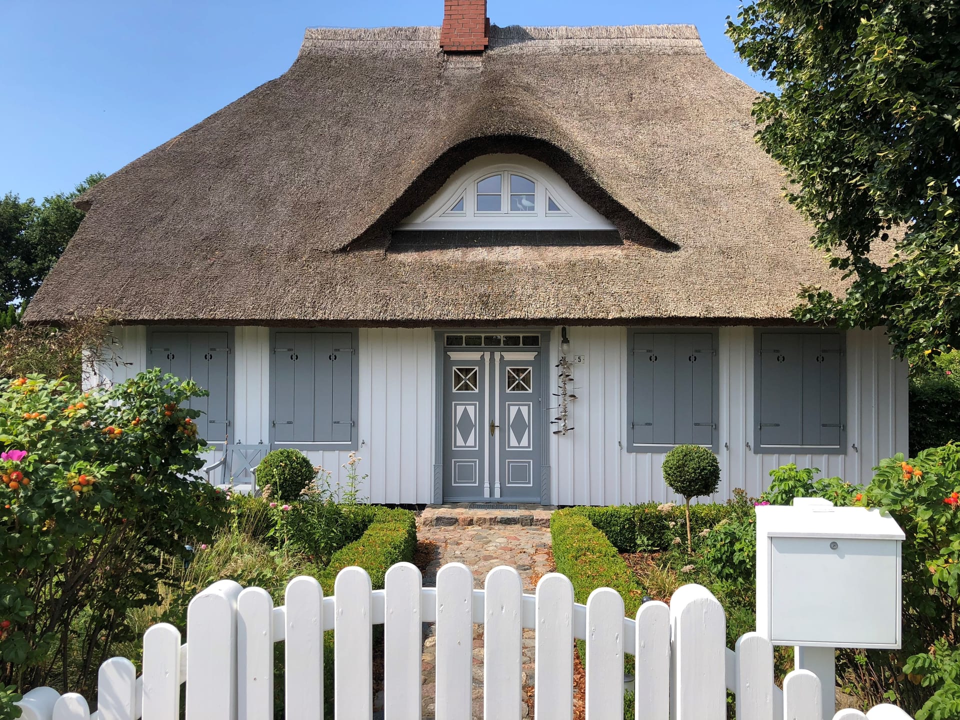 Reetgedecktes Haus mit weißem Zaun und gepflegtem Bauerngarten