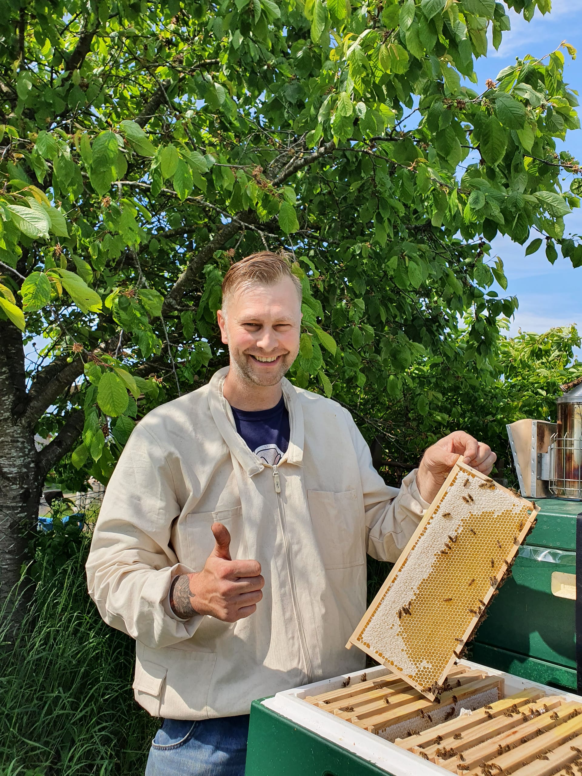 Imker zeigt Honigwabe am Bienenstock und lächelt zufrieden