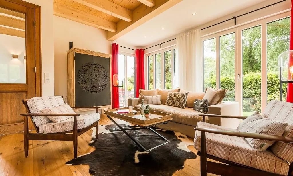 Wohnzimmer mit Holzdecke, Kamin, rotem Vorhang und gemustertem Sessel