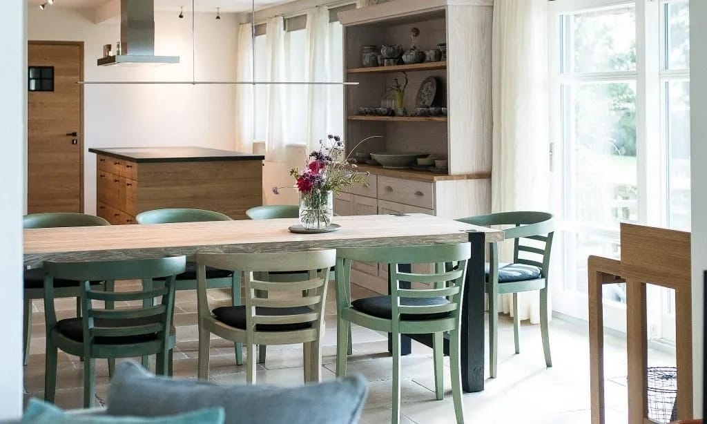 Esstisch mit grünen Stühlen, Blumenstrauß und offener Küche