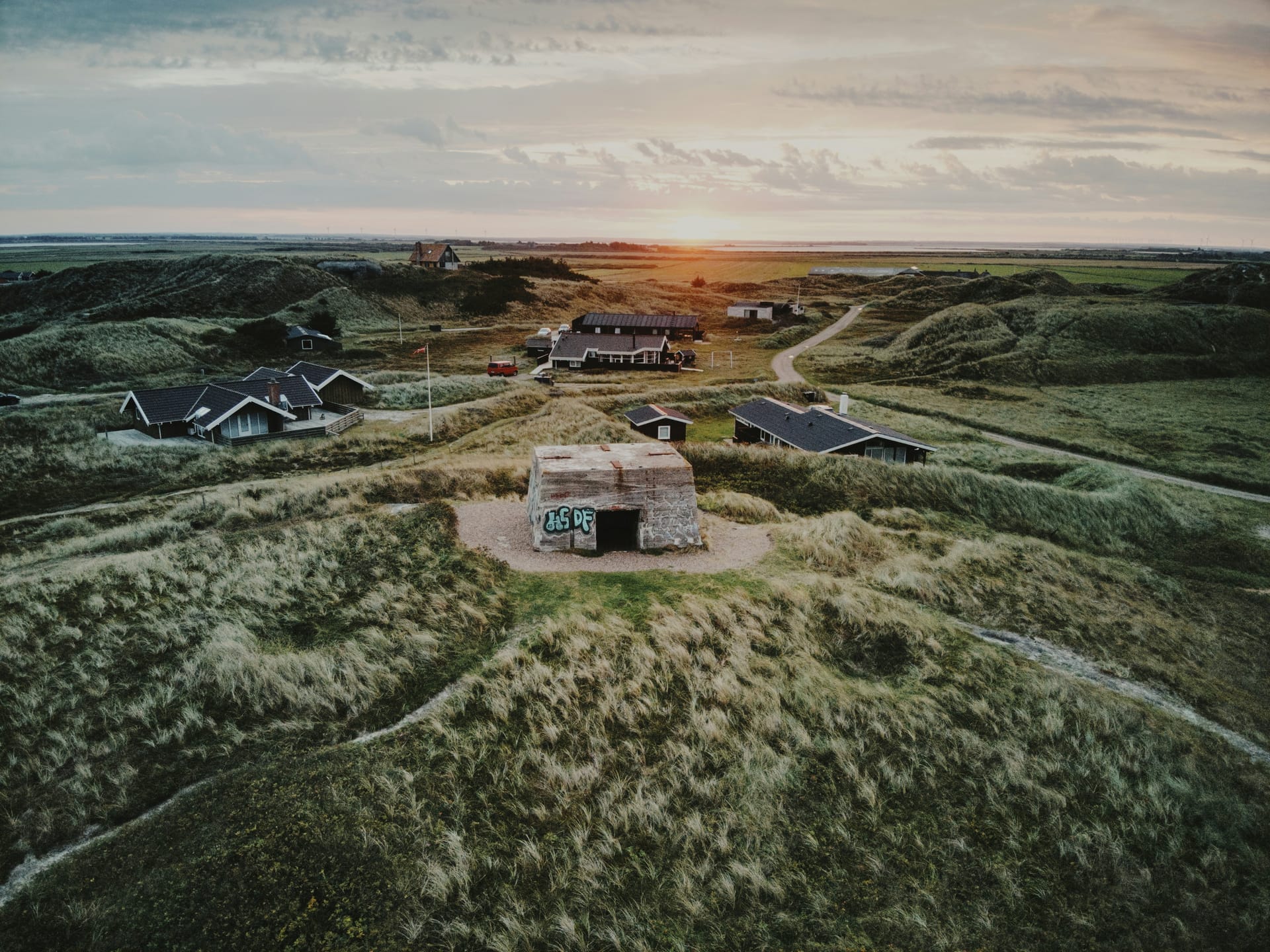 Luftaufnahme eines alten Bunkers in den Dünen mit Ferienhäusern im Sonnenuntergang.