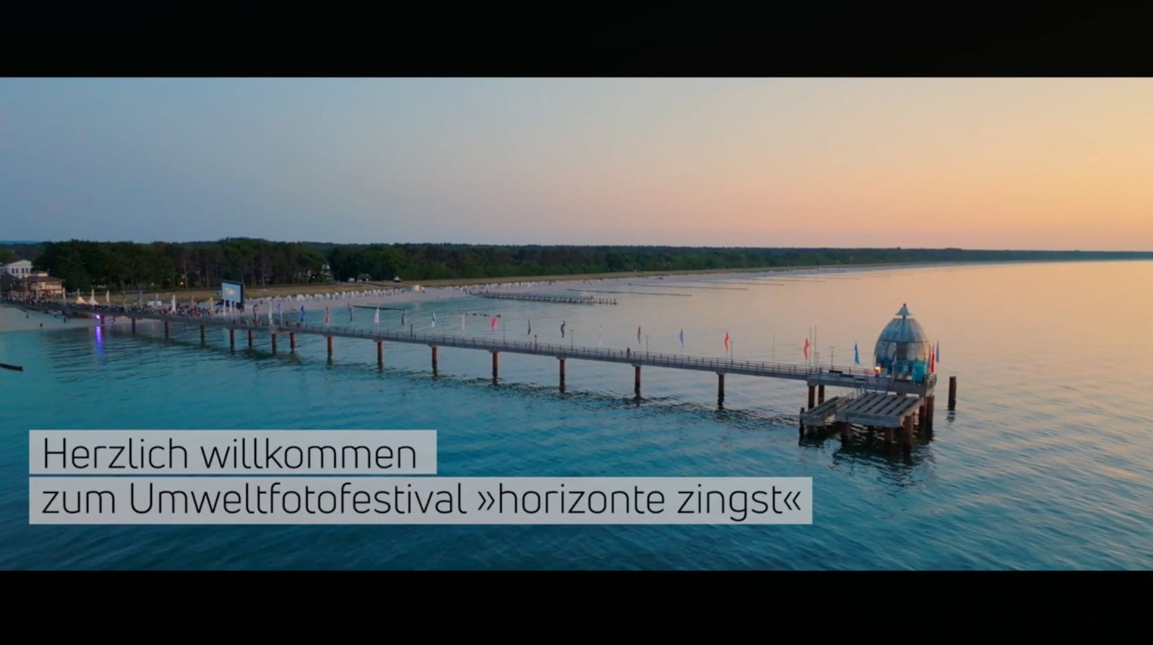 Luftaufnahme der Seebrücke Zingst bei Abenddämmerung mit Schriftzug zum Umweltfotofestival.