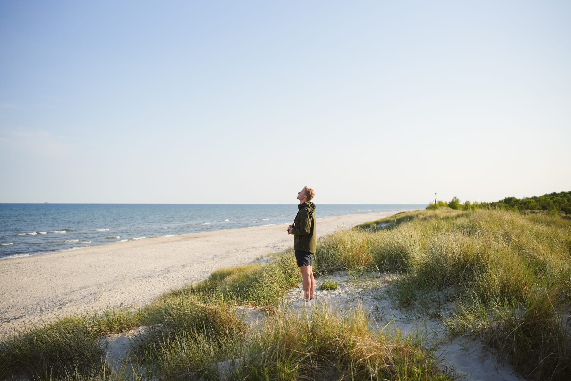Mann steht in den Dünen und blickt aufs Meer