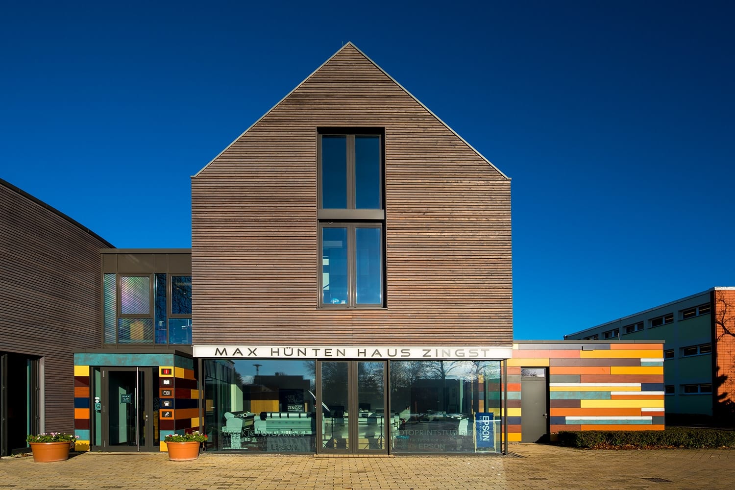 Modernes Max Hünten Haus in Zingst mit Holzfassade und bunten Elementen unter blauem Himmel.
