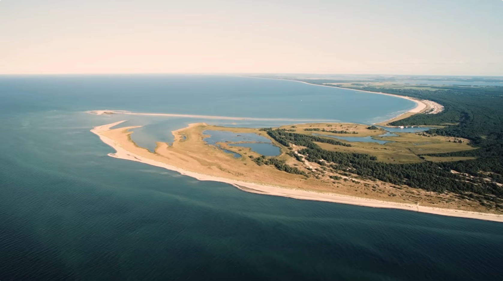 Luftbild einer schmalen, sandigen Landzunge im weiten, blauen Meer.